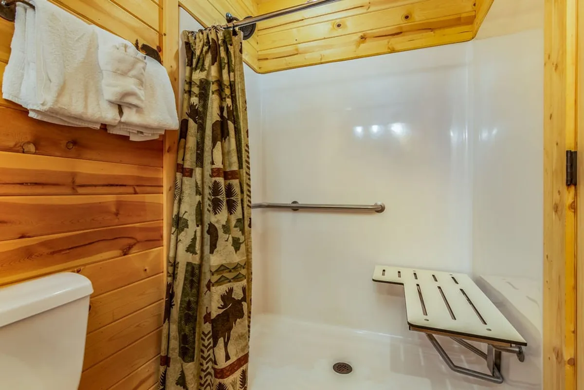 A welcoming bathroom with natural wood walls, a nature-themed shower curtain, and a folding shower bench. The space conveys a sense of relaxation and offers practical touches for a refreshing experience after a day of adventure.