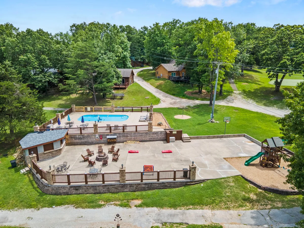 A lively scene featuring a swimming pool adorned with lounge chairs, a playground, and a basketball hoop—all framed by leafy trees. The multipurpose area is buzzing with activity, offering multiple opportunities for family enjoyment.