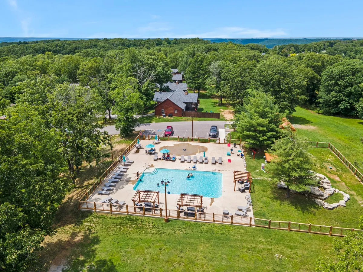 A sun-drenched swimming pool area surrounded by lounge chairs, lush greenery, and cabana structures, with people swimming, sunbathing, and socializing. The relaxed yet cheerful vibe makes it the perfect spot for group relaxation or celebratory gatherings.
