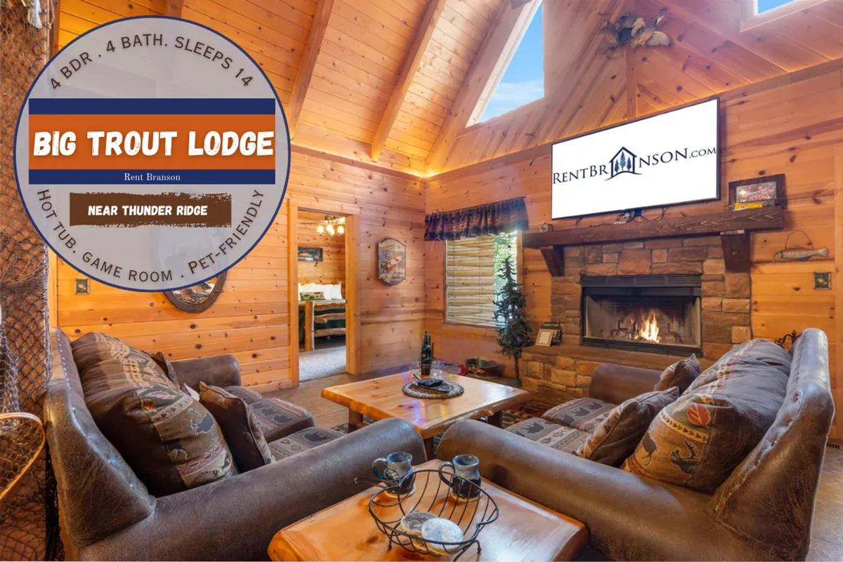 A cozy living area with a stone fireplace, large windows, exposed wooden beams, comfortable seating, and a TV. The room radiates warmth and is set up for group gatherings, relaxation, and shared movie nights.