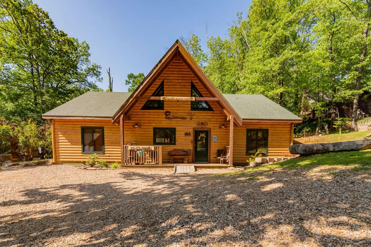 The hero image showcases the exterior of a classic log cabin nestled in lush greenery, with a welcoming front porch lined with comfortable seating. A stone pathway leads guests up to the cabin, inviting them to relax outdoors or gather under the trees. The scene is set during the golden hour, highlighting the warm sunset glow, and hints at tranquil mornings with coffee or cozy evenings around a campfire.