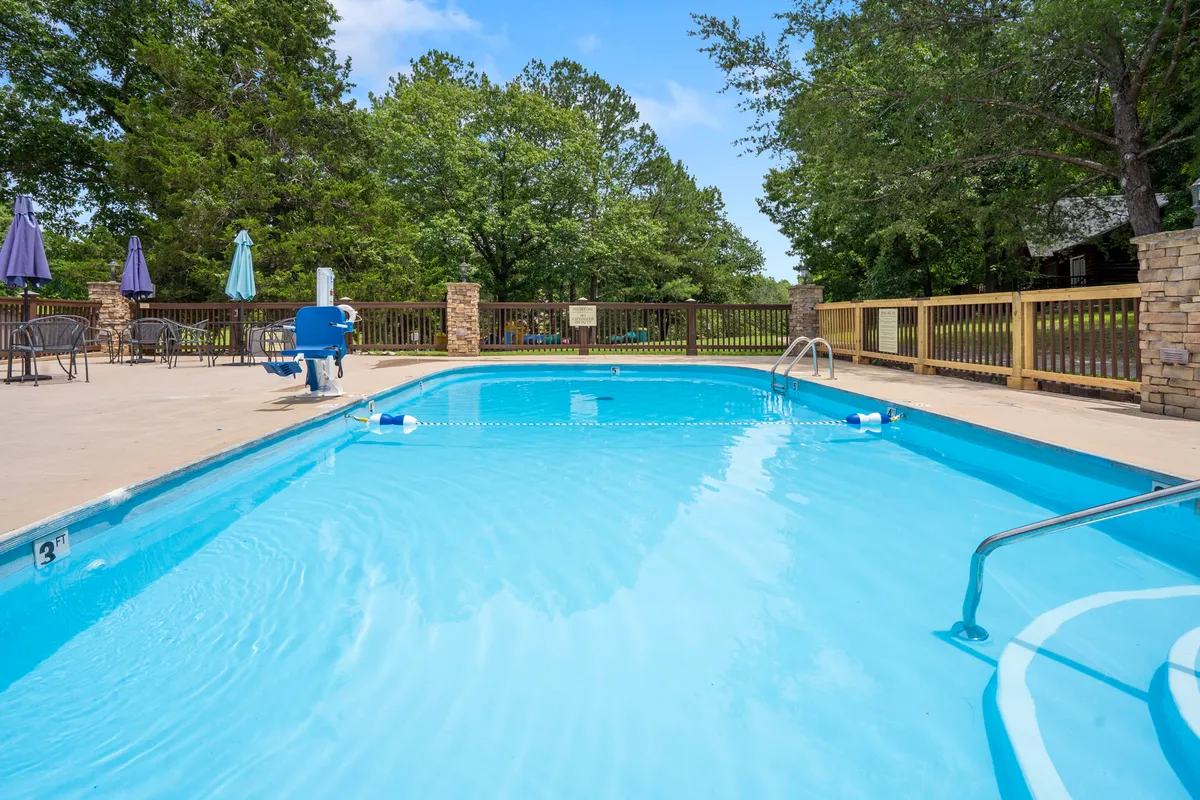 A sunlit swimming pool surrounded by trees, poolside furniture, and fencing, welcoming guests for a refreshing dip. The inviting pool area represents the resort amenities available to guests just steps from the cabin.