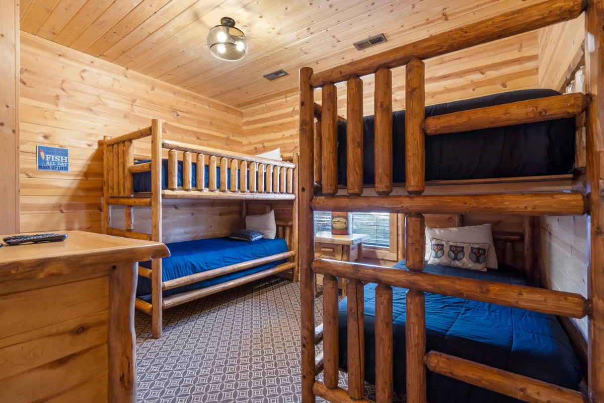 A charming bunk room featuring two sets of sturdy wooden bunk beds with cozy bedding and playful textiles. The space feels inviting and is clearly designed with kids or teens in mind, with warm lighting and practical details.