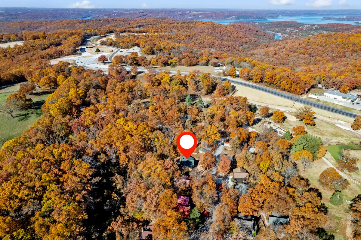 A winding road curves through dense, vibrant autumn trees, leading toward a distant glimpse of a water body. The lush foliage and road create an inviting scene, perfect for scenic drives to and from the lake or marina, encapsulating the joy of exploring the Ozarks outdoors.
